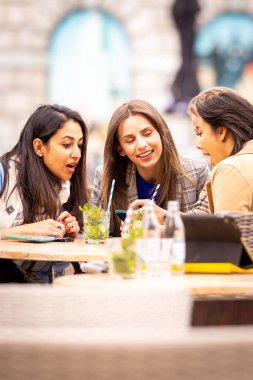 Three friends engage in a lively conversation at an outdoor cafe, enjoying drinks and each others company in the city clipart