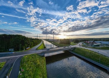 Halle, Belçika, 9 Temmuz 2024 otoyol köprüsü, kanal, rüzgar türbinleri ve bulutlu pitoresk gökyüzü üzerindeki günbatımının büyüleyici görüntüsünün tadını çıkarın.