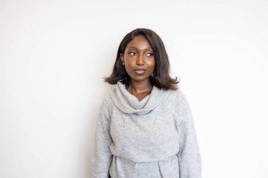 Gri kazaklı şık, kendine güvenen bir kadın beyaz bir arka plana karşı duruyor. Profesyonel zarafet ve tarz yayıyor.