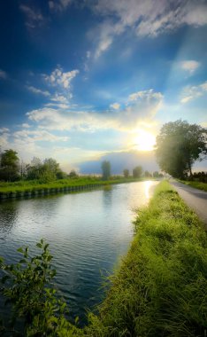 Huzurlu bir nehir manzarası canlı bir gündoğumu ile sergileniyor yemyeşil bankaları ve manzarayı aydınlatan