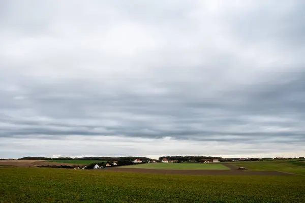 stock image A wide expanse of lush fields and distant farmhouses under a dramatic overcast sky, portraying a serene rural landscape