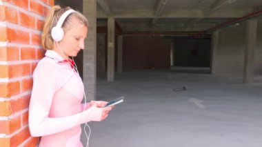 Şık, pembe bir kıyafet giyen genç bir kadın, çağdaş bir şehir ortamında telefonuyla müziğin keyfini çıkarıyor.