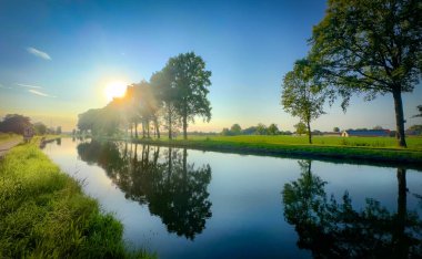 Güzel, sakin bir manzara sergiliyor çarpıcı bir günbatımını bereketli ağaçlarla kaplı huzurlu bir nehire yansıtıyor.