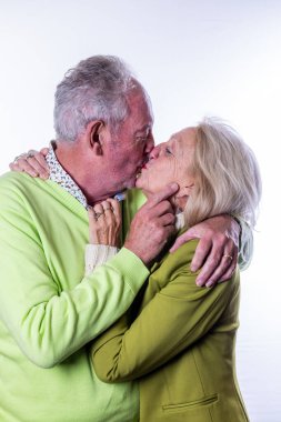 An elderly couple sharing a tender kiss in colorful attire, showcasing their love and deep affection clipart