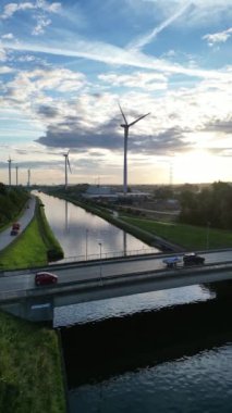 Sersemletici rüzgar türbinlerini sakin bir kanalda, canlı bir günbatımı gökyüzünün altında renklerle dolu