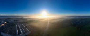 A breathtaking sunrise brilliantly illuminating a misty landscape adorned with captivating industrial structures below clipart