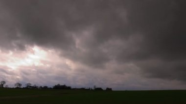 Canlı yeşil bir tarlanın üzerindeki koyu renkli bulutların manzarası doğayı, ham yoğunluğu ve güzelliği yakalıyor.