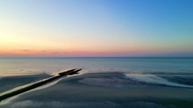 Gün batımında sakin ve huzurlu bir deniz manzarası. Yumuşak renkler ufku sıcacık renklerle kaplıyor.
