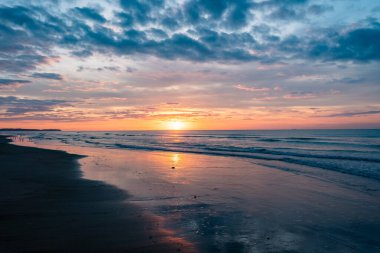 Sakin bir sahil gün batımını canlı renkler ve sakin dalgalarla deneyin. Deniz kenarında sakin bir akşam için idealdir.