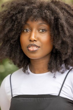 Doğal bukleleri olan kendine güvenen bir kadın dışarıda güneşlenirken güzellik ve tarz yayar.