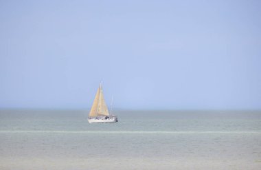 Uçsuz bucaksız mavi gökyüzünün altında sakin sularda süzülen bir yelkenlinin güzel sakin manzarası.