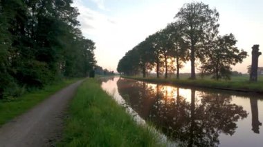 Huzurlu ve büyüleyici bir kanal yolu. Huzurlu bir günbatımının altında güzel yansımalar ve canlı yeşillikler var.