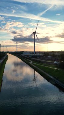 Su kenarında rüzgar türbinleriyle baş döndürücü bir gün batımı yenilenebilir enerji ve doğanın güzelliğini gösteriyor.