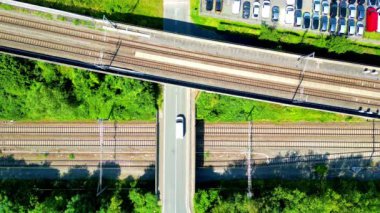 Yeşilliklerle çevrili yolları ve demiryollarını birbirine bağlayan etkileyici bir üst geçidi gösteren hava görüntüsü.
