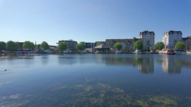 Turnhout, Belçika, 14 Haziran 204 berrak mavi gökyüzü altındaki binalarla birlikte sakin ve resimli bir göl manzarası sergiliyor.