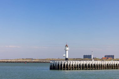Güneşli bir günde sakin ve sakin sulara bakan ahşap bir iskelede gururla duran pitoresk bir deniz feneri.