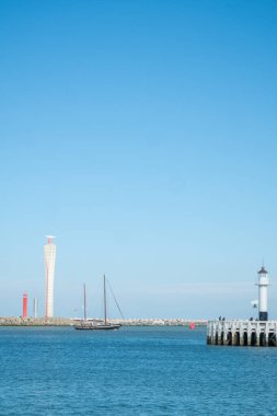 Oostend, Belçika, 6 Ekim 2024 çarpıcı bir deniz feneri, zarif yelkenliler ve açık mavi bir gökyüzü gösteren çarpıcı ve sakin bir kıyı manzarası.