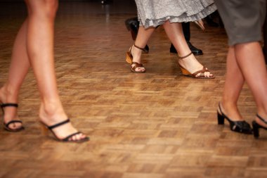 Canlı ve hayat dolu bir sahne, zarif ayaklar, parlak ahşap bir zeminde şık, kayışlı topuklarla dans ediyor.