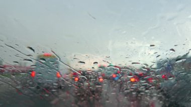 Yağmurlu bir ön camda yoğun trafiğin bulanık görüntüsü, güzel bir şekilde ışık yansımaları sergiliyor.