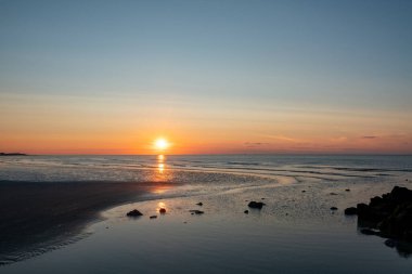 Nefes kesici ve renkli bir gün batımı, engin okyanusu aydınlatıyor, sakin ve huzurlu bir sahil atmosferi yaratıyor.