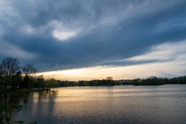 Karamsar ve dramatik bulutlar sergilerken alacakaranlığın ılık parıltısını yakalayan güzel sakin bir göl sahnesi.