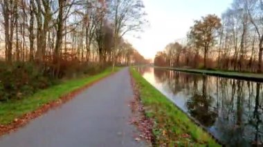 Renkli yapraklarla süslenmiş, gün batımında çarpıcı güzellikleri yansıtan sakin bir kanal yolu.