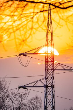 A stunningly beautiful sunset creates a silhouette against the power lines and a towering transmission structure clipart