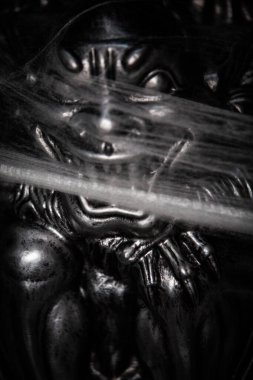 Bu karanlık, desenli bir heykelin büyüleyici bir yakın görüntüsü entrika ve derin bir derinliği çağrıştırıyor.