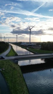 İnanılmaz güzel bir manzara, nefes kesen bir gökyüzünün altında sakin bir nehrin yanında yer alan rüzgar türbinlerini sergiliyor.