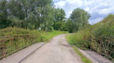 Bulutlu bir gökyüzünün altında büyüleyici kırsal köprüler ve canlı, yemyeşil bir bitki örtüsüyle çevrili huzurlu ve sakin bir yol.