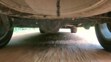 Asfaltsız ve engebeli bir yolda ilerleyen bir arabanın iniş takımının detaylı bir yakın plan görüntüsü.