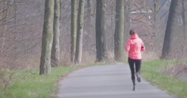 Uzun ve gür ağaçlarla çevrili sakin ve huzurlu bir yolda koşan bir birey.