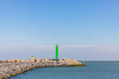 Oostend, Belçika, 6 Ekim 2024, büyüleyici yeşil bir deniz feneri deniz kıyısındaki kayalık bir iskelede, parlak mavi gökyüzüne karşı yükseldi.