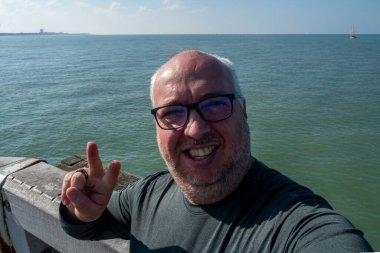 Neşeli ve neşeli bir birey, arka planda güzel okyanus dalgalarıyla canlı bir selfie çeker.