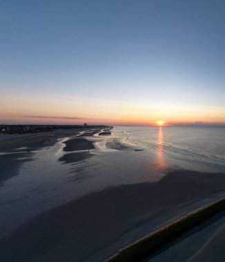 Canlı bir gün batımı sakin bir sahildeki sakin suları güzel bir şekilde yansıtır. Derin bir huzur ve sükuneti çağrıştırır.