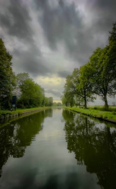 Bereketli yeşilliklerin, bereketli ağaçların ve gerçek güzelliği yansıtan karamsar bulutların olduğu sakin bir nehir manzarası.