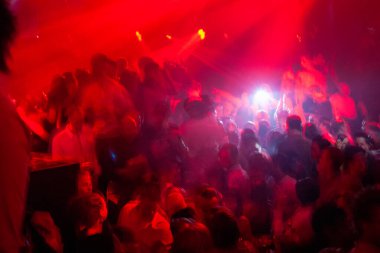 Göz kamaştırıcı kırmızı ışıkların altında dans eden kalabalıklarla dolu canlı, canlı bir gece kulübü atmosferi.