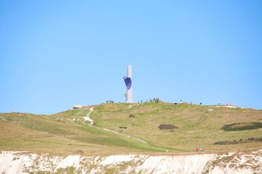 A monument stands tall on a hill under a clear blue sky, attracting many visitors eager for adventure clipart