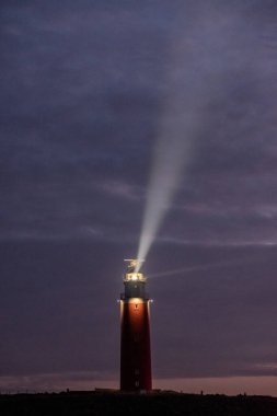 Eierland, De Cocksdorp, Texel, Hollanda, 28 Ekim 2024, çarpıcı bir deniz feneri ışık saçar alacakaranlık gökyüzüne, sakin bir kıyı sahnesi yaratır..