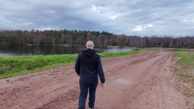 Bir insan, yemyeşil bir çevreyle çevrili güzel bir göl kenarında huzurlu bir yol boyunca sakin bir şekilde yürür.