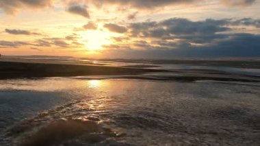 Güzel, canlı bir gün batımı yumuşak okyanus dalgalarına harika bir şekilde yansıyarak sakin ve sakinleştirici bir atmosfer yaratır.