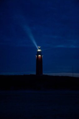 De Cocksdorp, Texel, Hollanda, 27 Ekim 2024, büyüleyici bir deniz feneri alacakaranlıkta karanlık gökyüzüne doğru ışık saçar ve güzel bir kontrastlık yaratır.