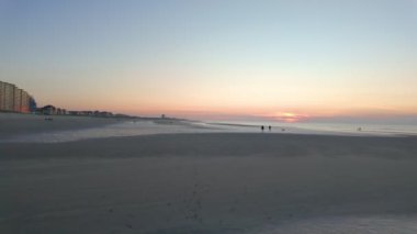 Nieuwpoort, Batı-Flanders, Belçika, 6 Ekim 2024 çarpıcı bir günbatımı manzarası, nazik dalgalar ve güzel bir atmosfer yaratan uzak bina siluetleri.