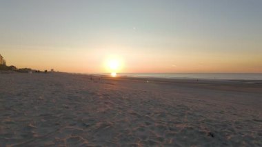 Huzurlu ve sakin bir sahil sahnesi güzel bir şekilde sergileniyor çarpıcı bir günbatımı yavaşça ufuktan aşağı iniyor.