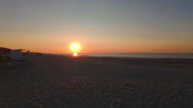 Resimli bir günbatımı, sakin plajı ve engin okyanusu güzel ve huzurlu bir şekilde aydınlatıyor.