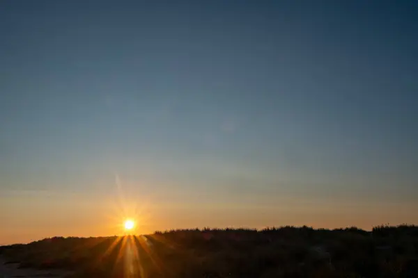 A serene and peaceful sunrise beautifully illuminating the vast sand dunes against a clear blue sky above