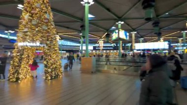 Schiphol Havaalanı, Amsterdam, Hollanda, 20 Aralık 2024, bir havaalanı terminalinde canlı bir tatil atmosferi, ışıklarla süslenmiş, hareketli gezginler ve neşeli bir ağaç..