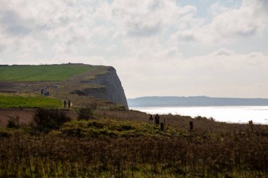 Doğanın güzelliklerinin arasında sakin bir şekilde yürüyen insanların olduğu nefes kesici ve resimli bir sahil kayalığı manzarası.