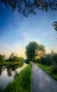 Canlı yeşilliklerle çevrili, dingin bir kanal yolu şafak vakti nefes kesici güzellikler sergiliyor.
