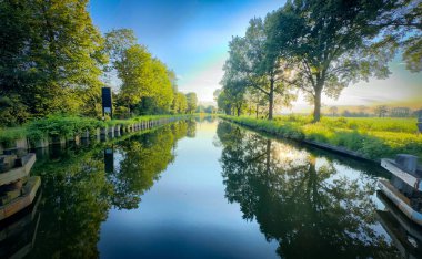 Şafak vakti berrak ve güzel bir gökyüzünün altında yemyeşil, gür ve canlı bir nehir manzarası.